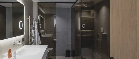 Un baño moderno con un espejo grande, dos lavamanos, una bañera y una zona de ducha con mampara de vidrio.