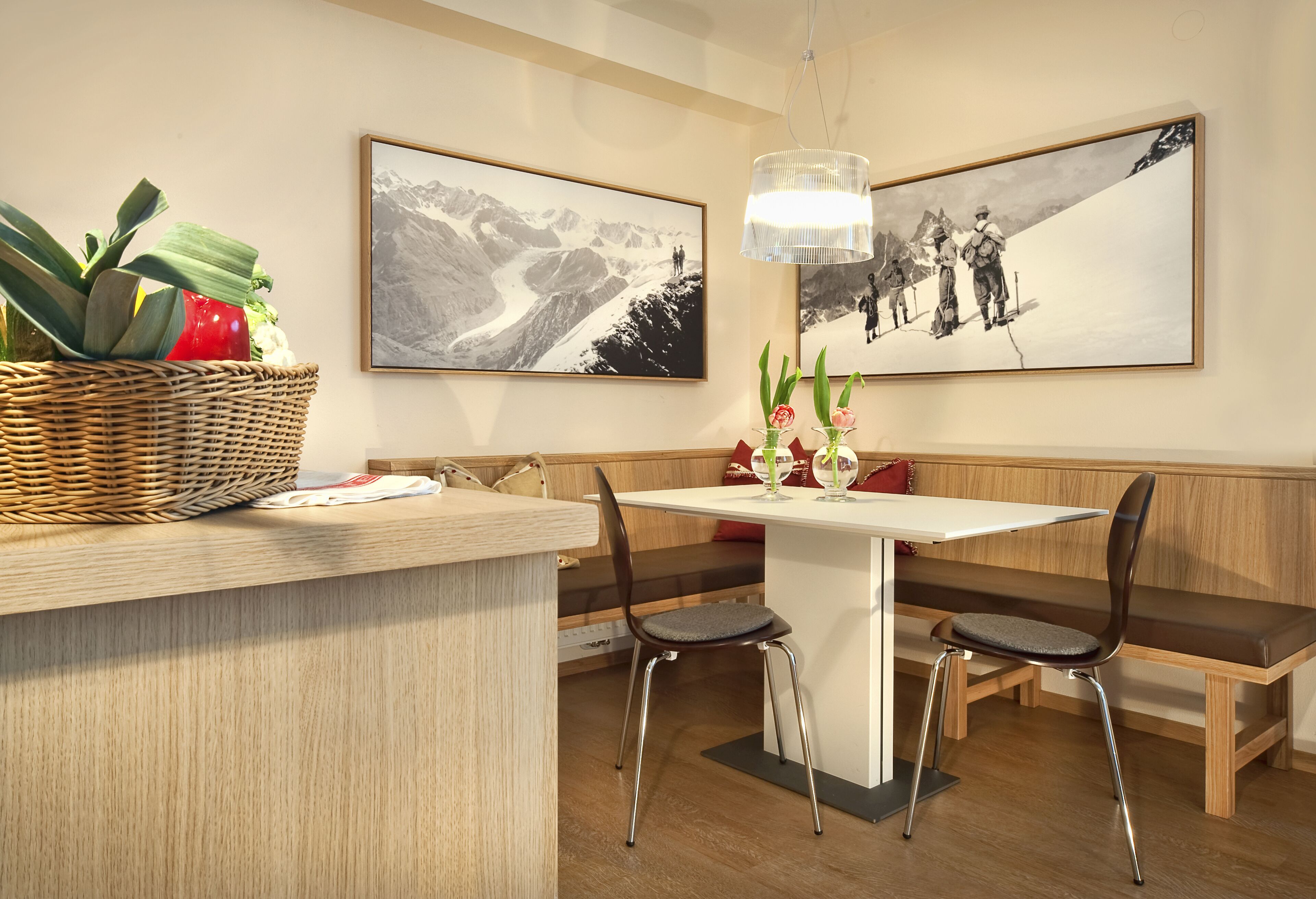 A dining area with a white table, two chairs, a bench, and a wicker basket with fruits and vegetables.