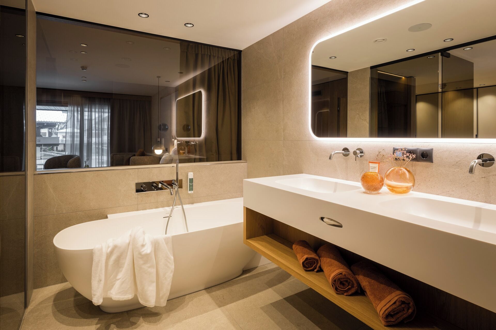 Un baño moderno con una bañera independiente, un espejo grande y un tocador con lavamanos y toallero.