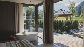 Une salle de bain moderne avec une baignoire sur pieds, une grande fenêtre et une vue sur un jardin et des montagnes.