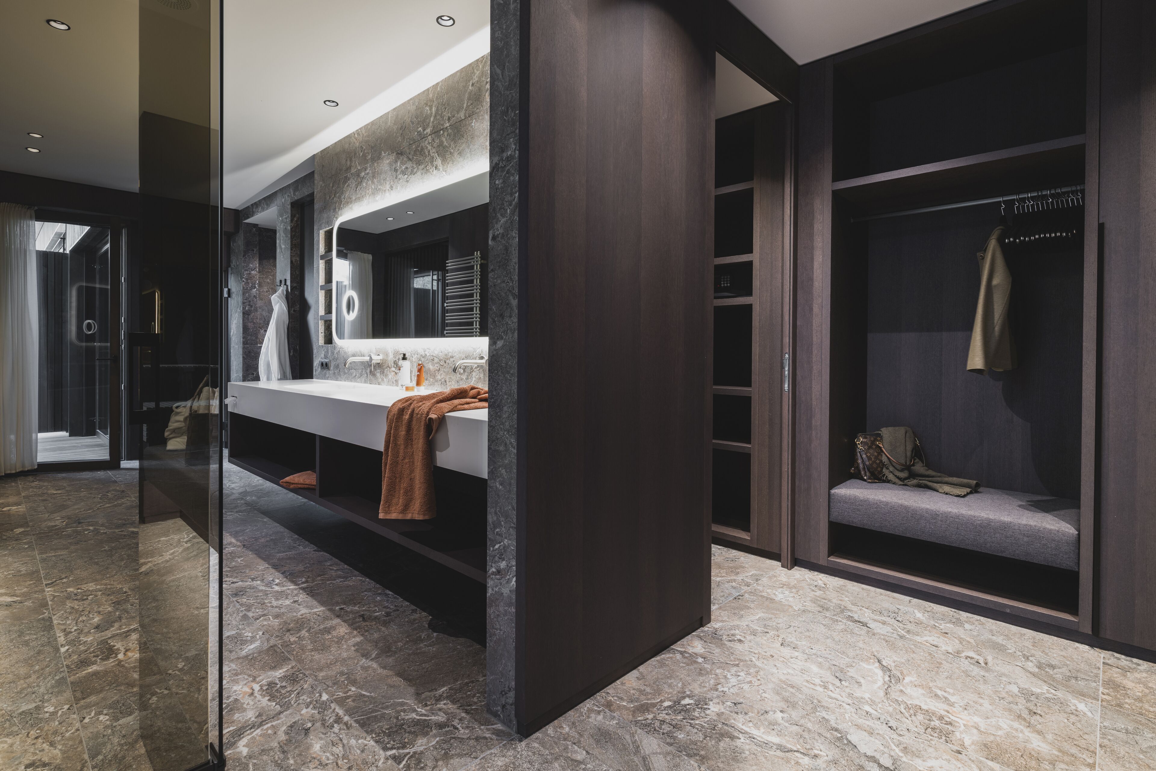 Un baño moderno con encimera de mármol, un espejo grande y una zona de estar integrada con una toalla.
