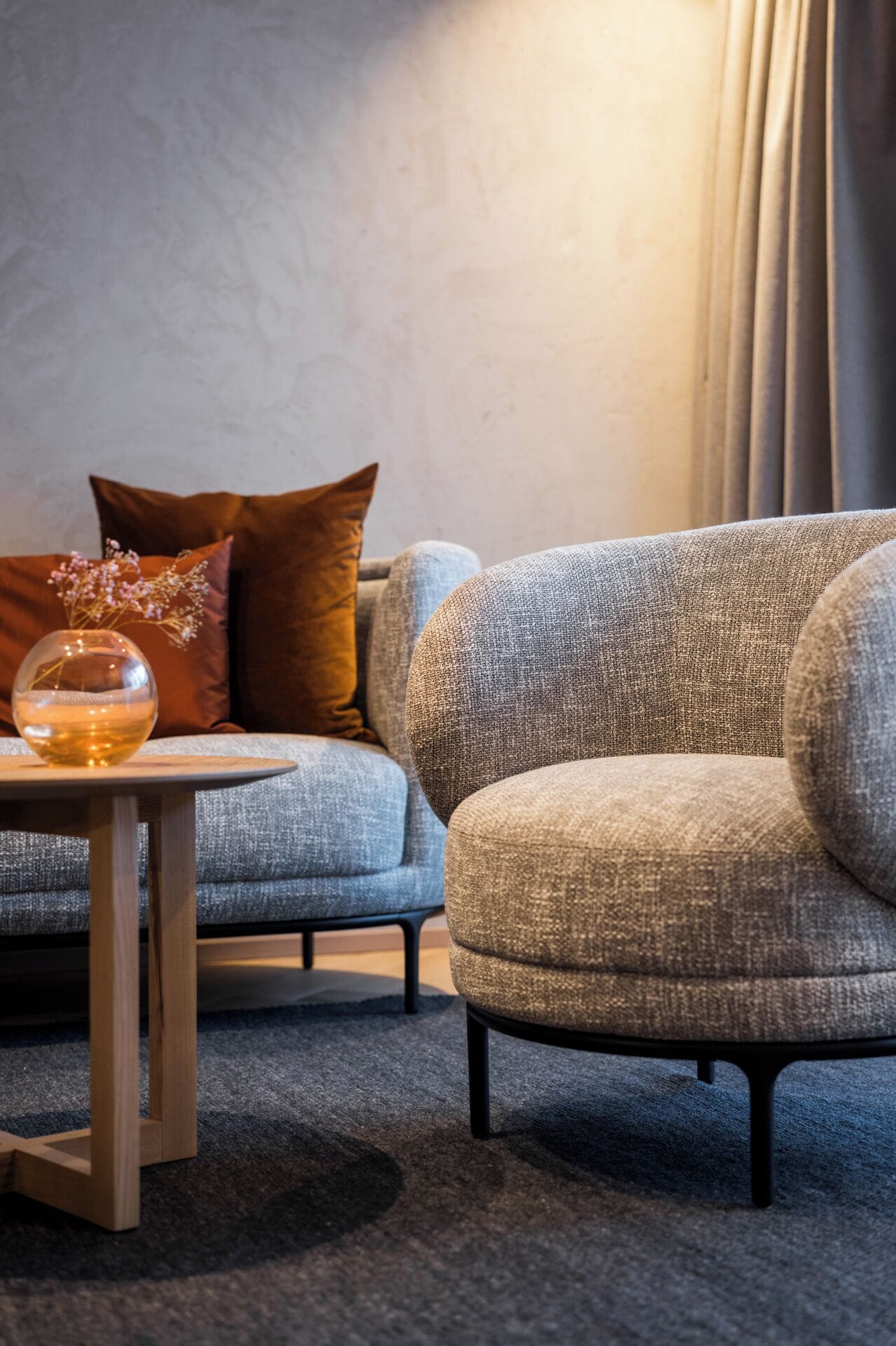 Ein modernes Wohnzimmer mit einem grauen Sofa, einem runden Holztisch und einer Vase mit Blumen.