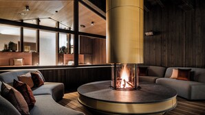 Un salon moderne doté d’une cheminée centrale de forme circulaire, de canapés et d’un plancher en bois.