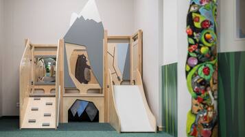 A children's play area with a wooden climbing structure, a slide, and a colorful wall mural.