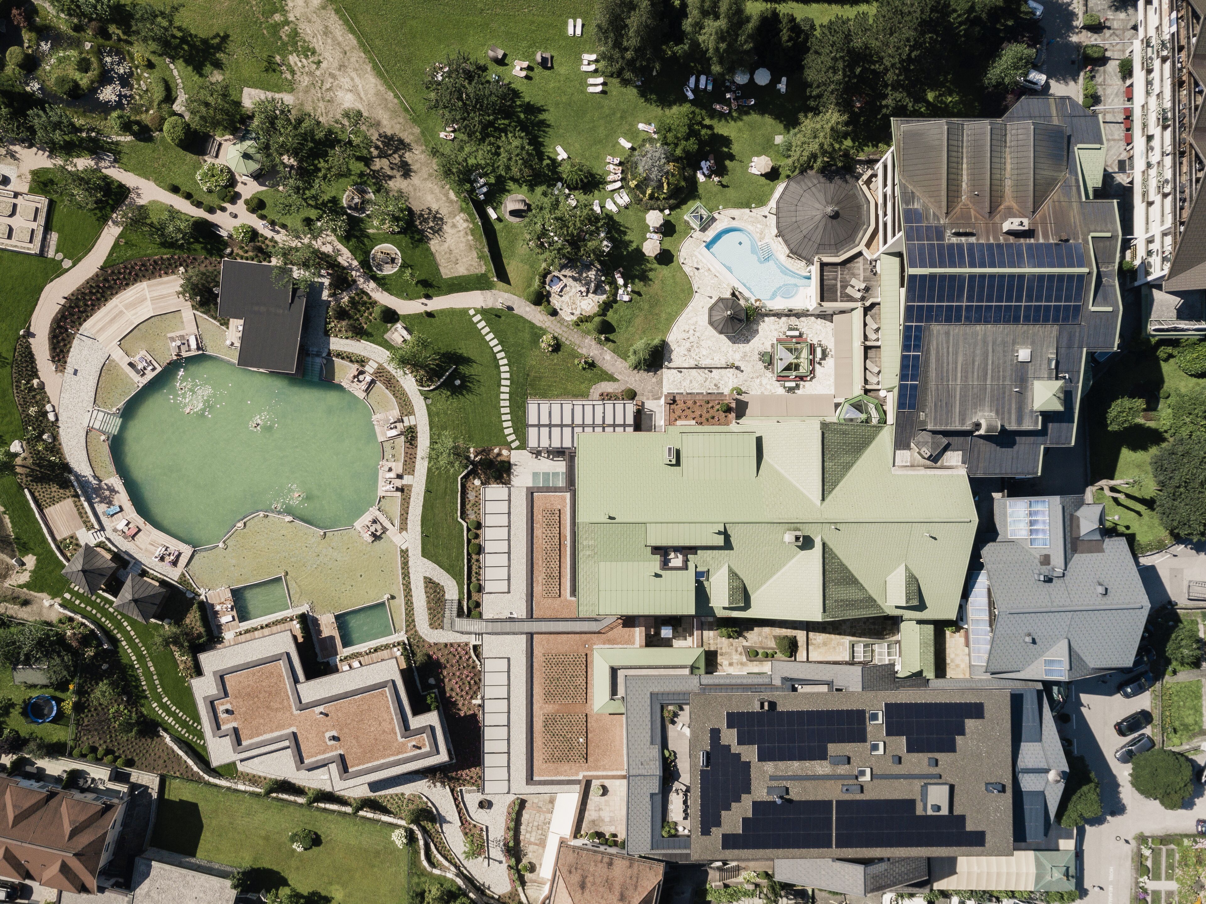 An aerial view of a residential area with a swimming pool, solar panels, and a tennis court.