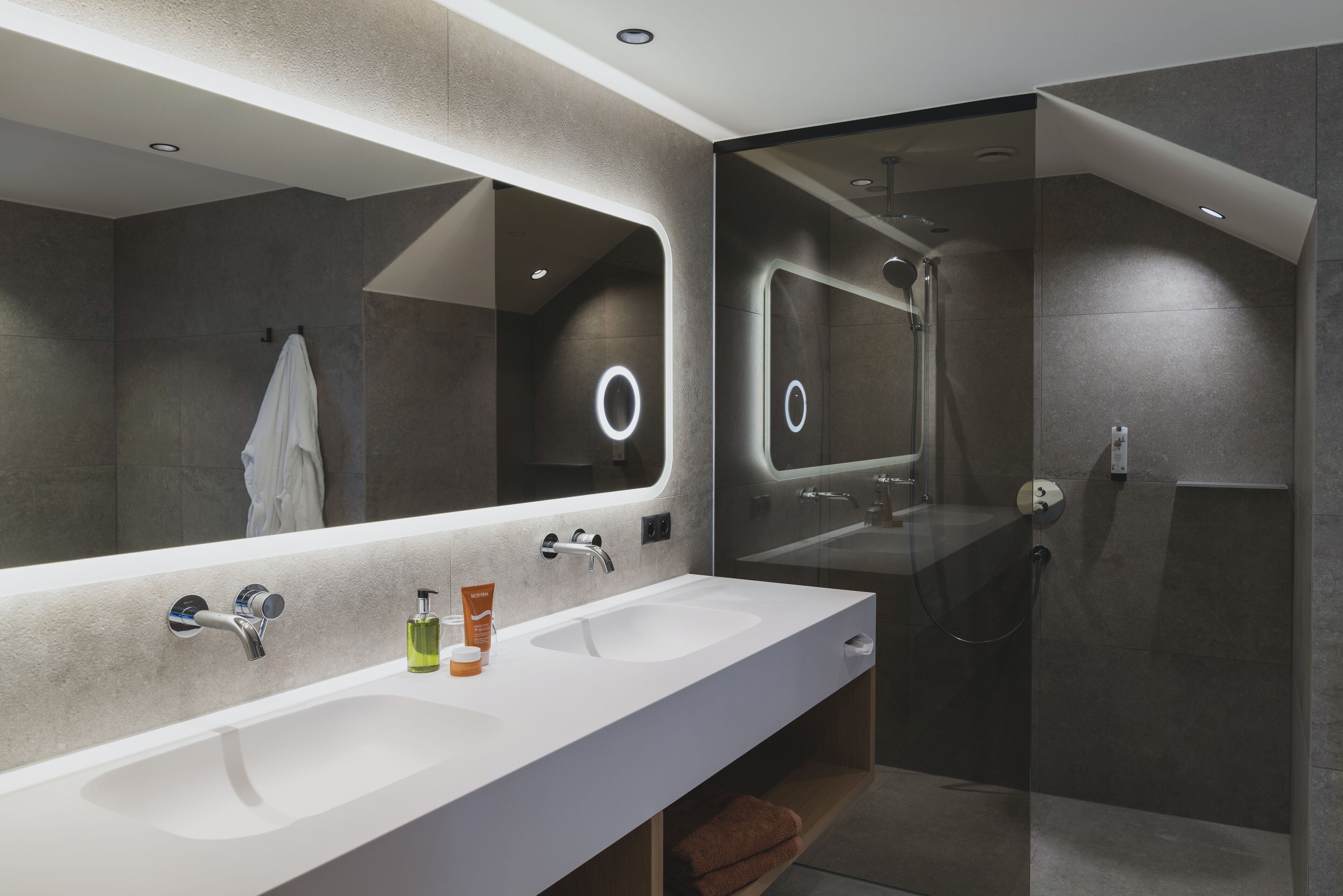 Une salle de bain moderne avec un grand miroir, deux lavabos et un espace douche.