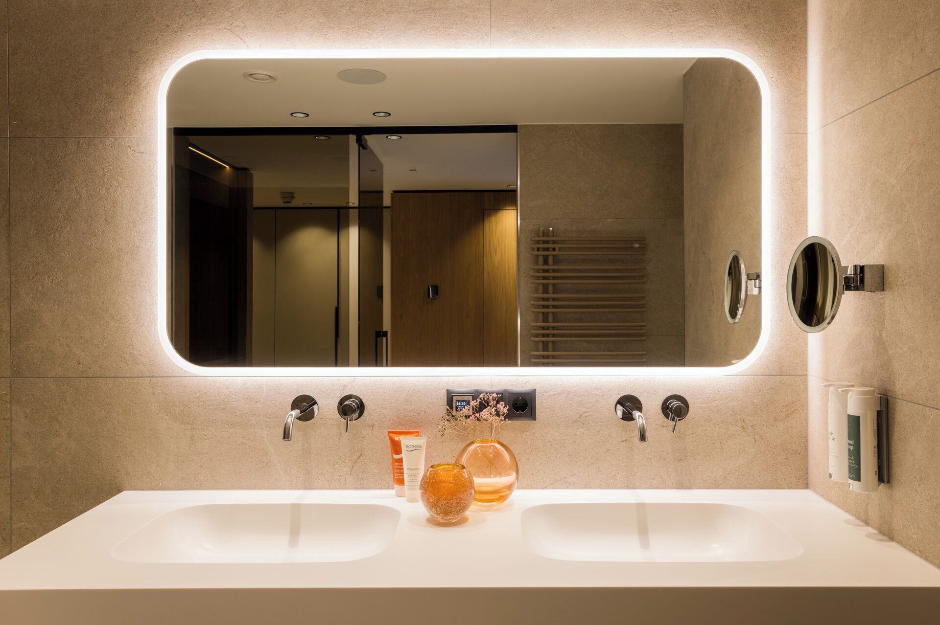 Une salle de bain moderne avec un grand miroir, deux lavabos et un porte-serviettes.