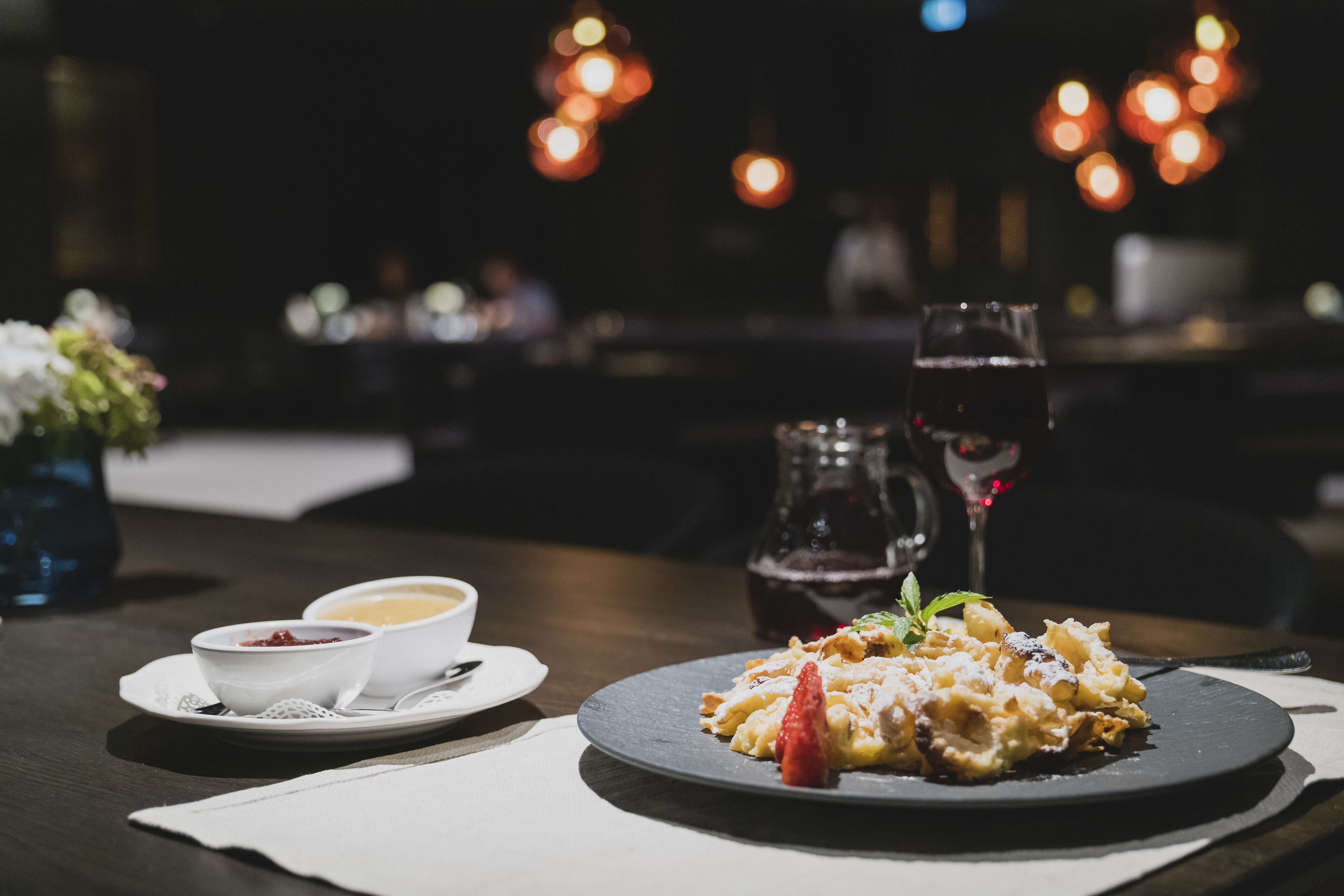 A dining table with a dessert plate, two bowls of soup, and a glass of red wine.