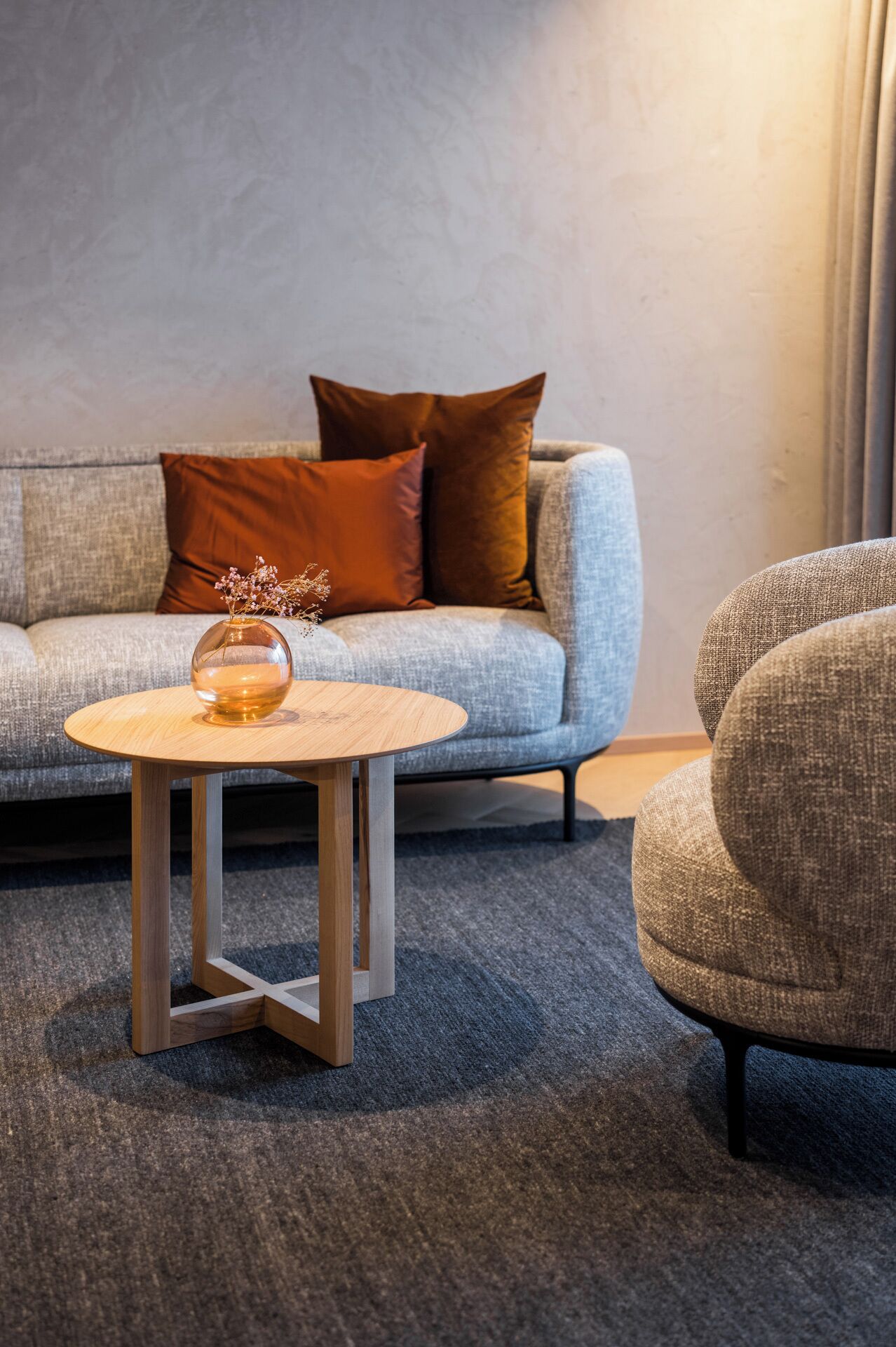 A modern living room with a grey sofa, a round wooden coffee table, and a grey armchair.