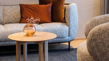 A modern living room with a grey sofa, a round wooden coffee table, and a grey armchair.