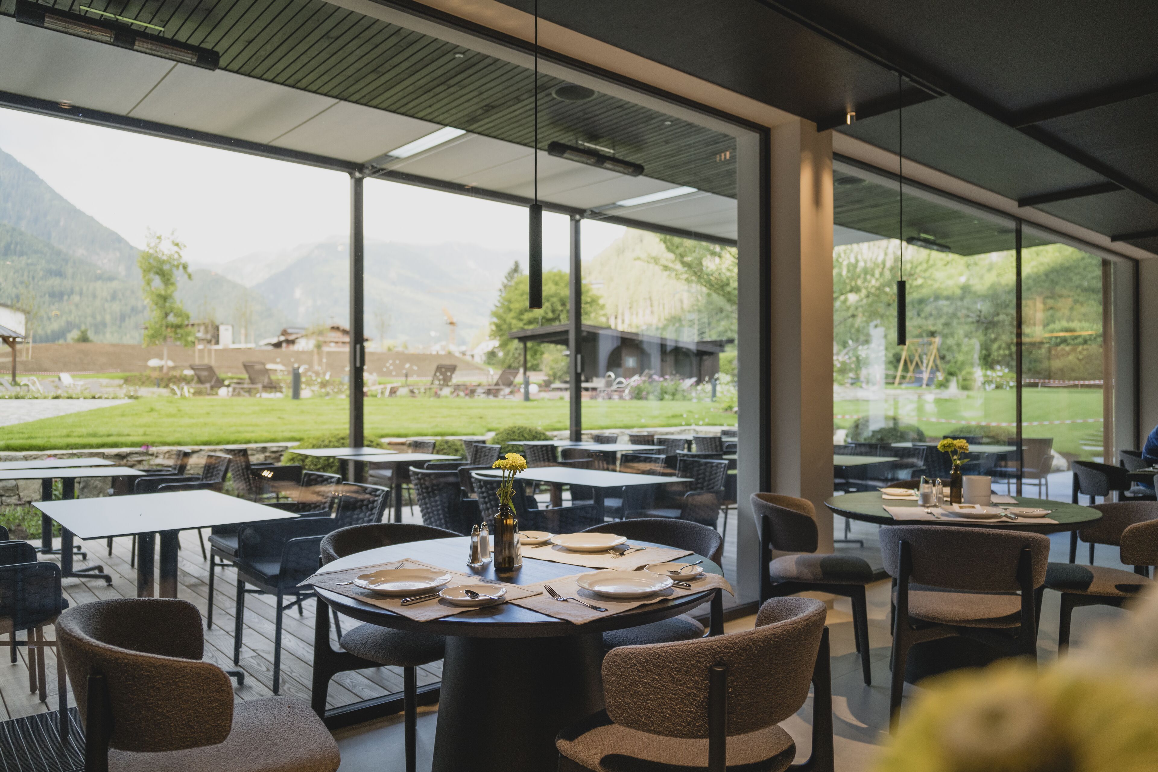 An outdoor dining area with tables and chairs, a view of mountains, and a glass wall.