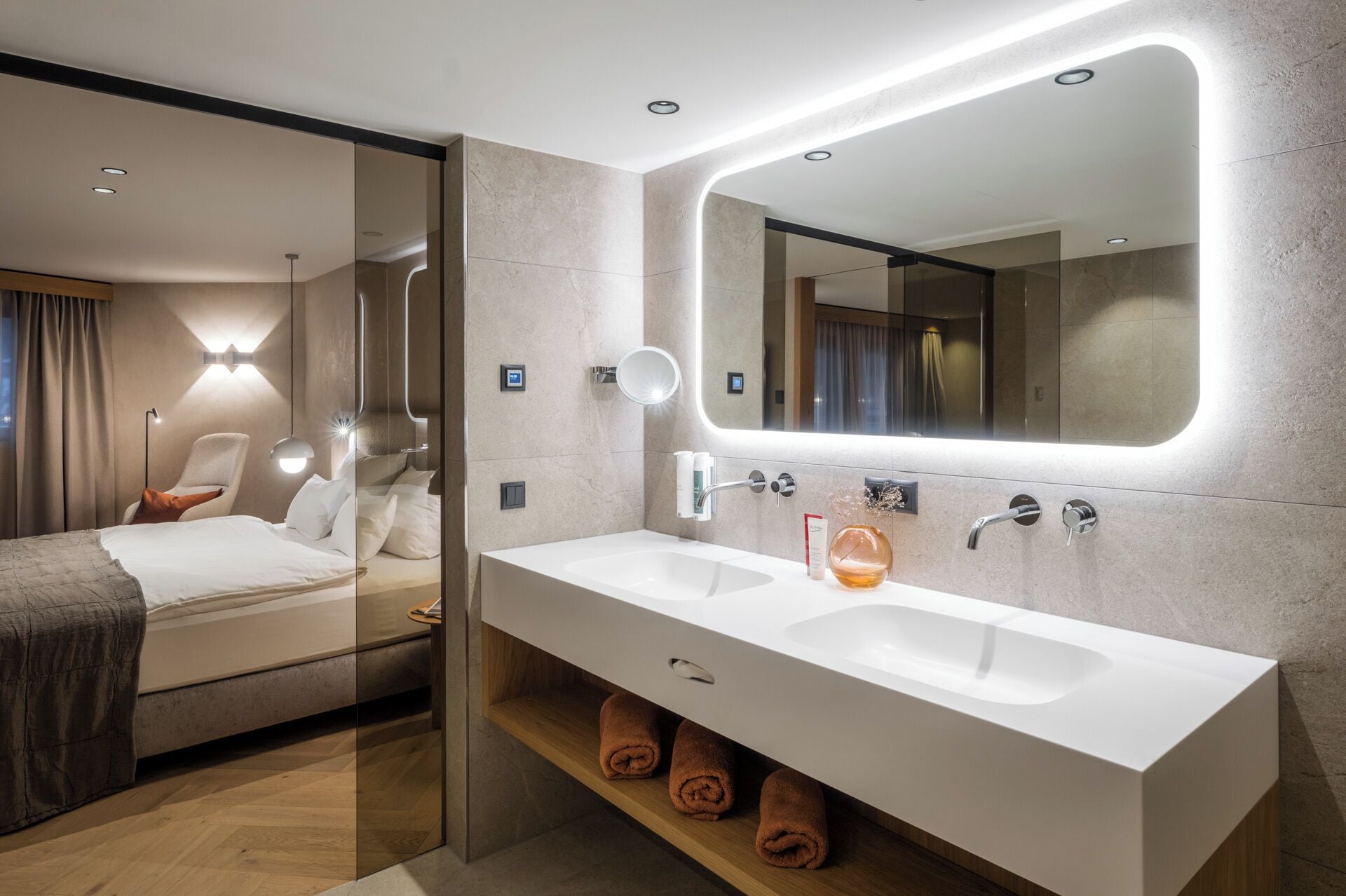 A modern hotel bathroom with a large mirror, dual sinks, and a glass-enclosed shower area.