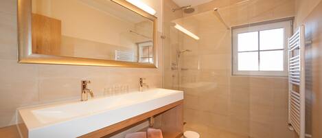 Une salle de bain moderne avec un grand miroir, un lavabo blanc, une douche et une fenêtre.