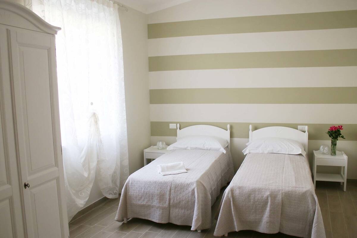 A bedroom with two single beds, a wardrobe, and a nightstand with a vase of flowers.