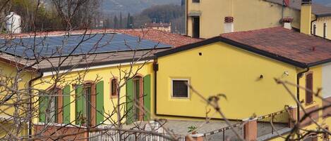 A yellow building with green shutters, a small window, and a balcony with a metal railing.