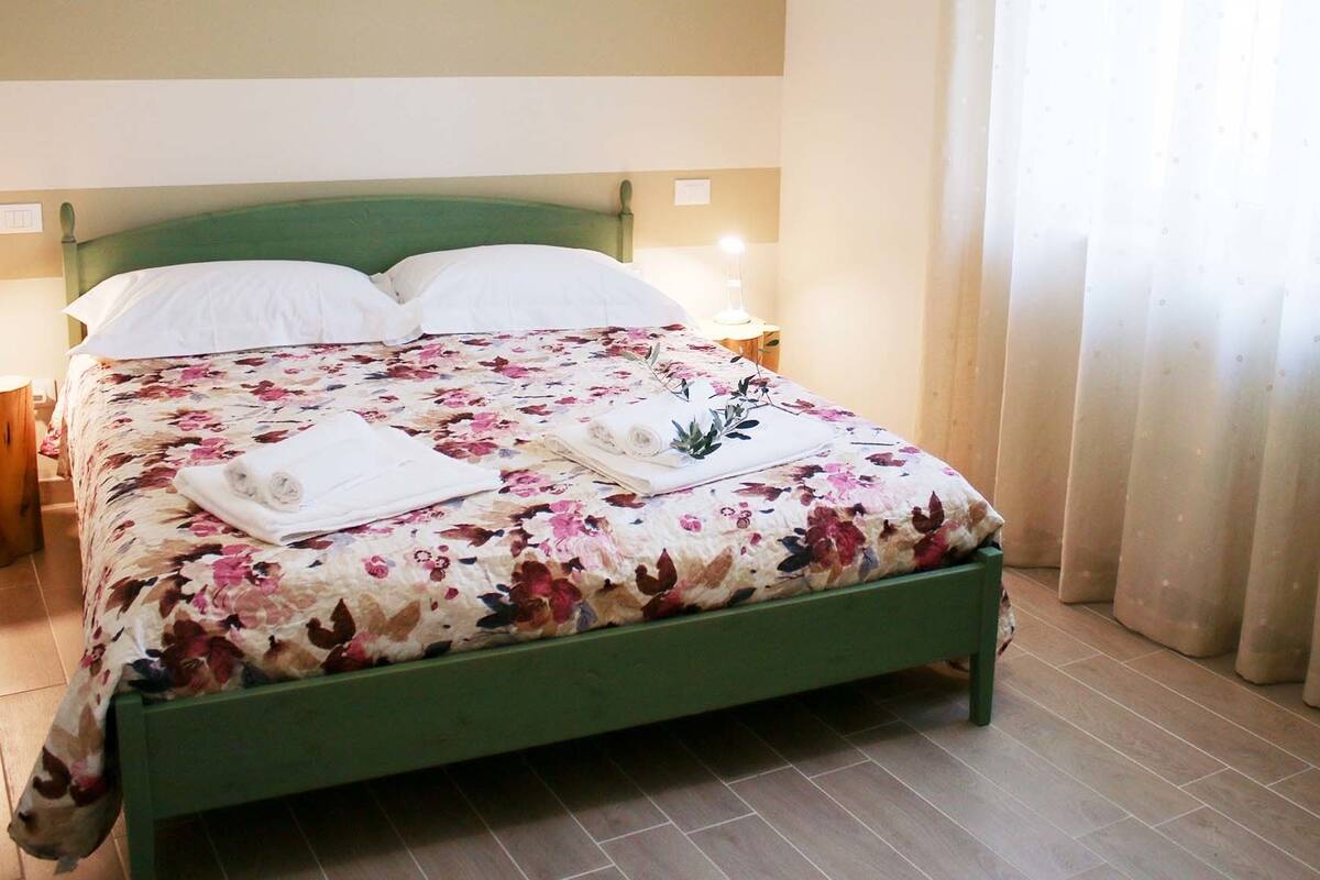A bed with a floral bedspread, two white pillows, and rolled towels on the bed.