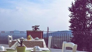 A table set for dining with a view of the sea, a potted plant, and a statue on a balcony. - B&B Corte Galo (Tregnago)