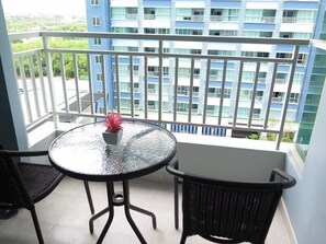 A balcony with a glass table and two chairs, overlooking a blue building with multiple windows. - Lumpini Parkbeach Jomtien Sea&Pool View by Dome (Pattaya)