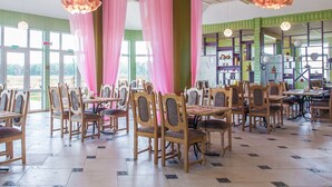 Un restaurante con sillas y mesas de madera, cortinas rosadas y lámparas florales colgantes.