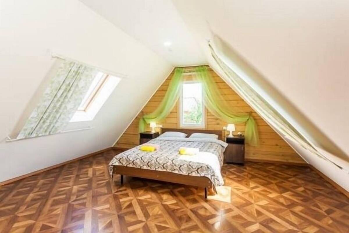 A bedroom with a sloped ceiling, a wooden floor, a bed with a patterned bedspread, and a window with curtains.