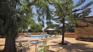 An outdoor pool area with lounge chairs and a table, surrounded by trees and a stone wall. - Agroturismo Finca Son Sureda (Manacor)