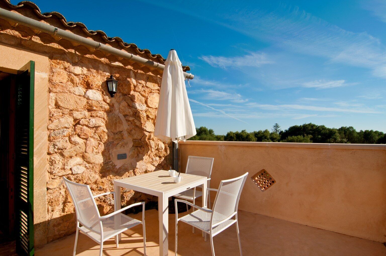 A patio with a table and chairs, a white umbrella, and a stone wall.