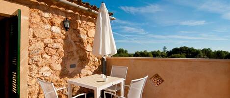 A patio with a table and chairs, a white umbrella, and a stone wall.