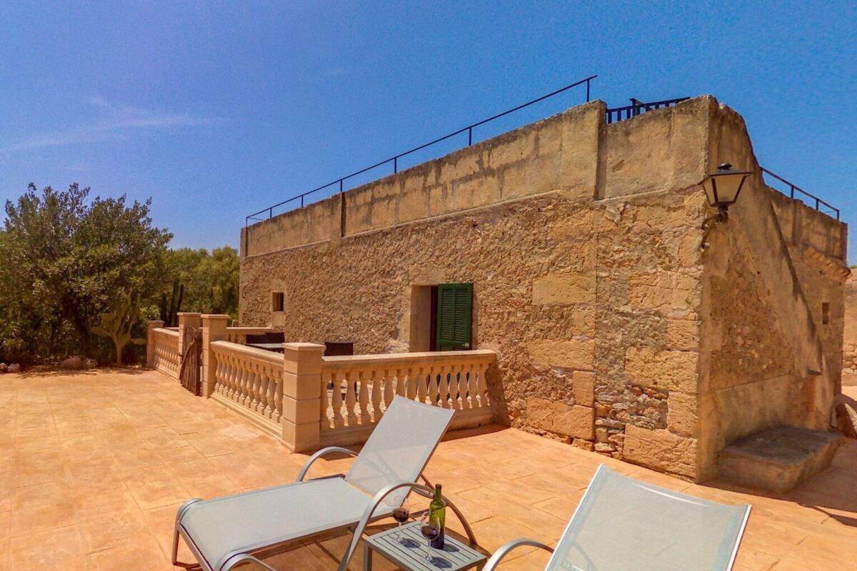 Un bâtiment en pierre doté d’un balcon, de deux fauteuils et d’une petite table sur laquelle se trouve une bouteille.