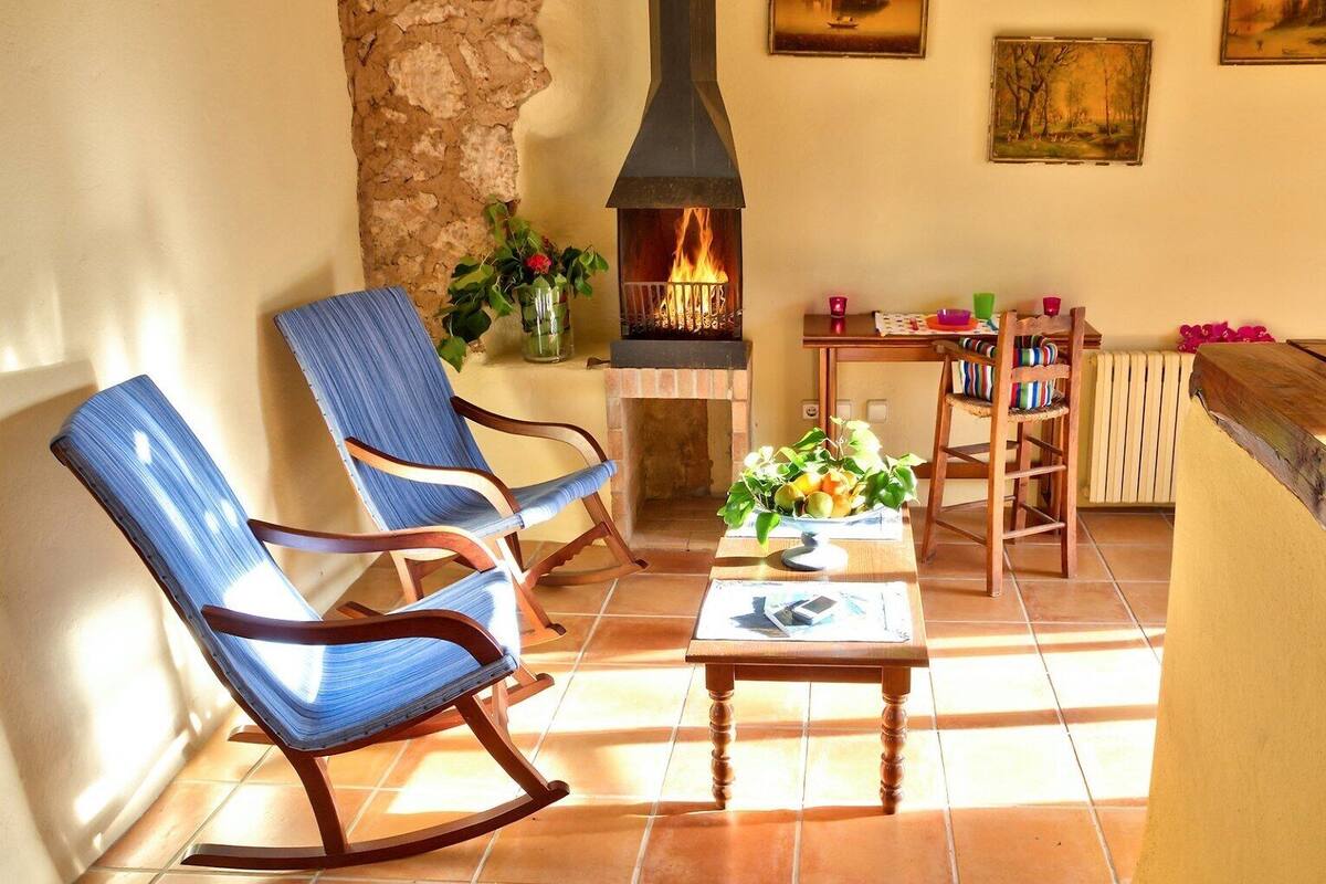 Un salon chaleureux avec deux fauteuils à bascule, une cheminée et une table ornée d’un vase de fleurs.