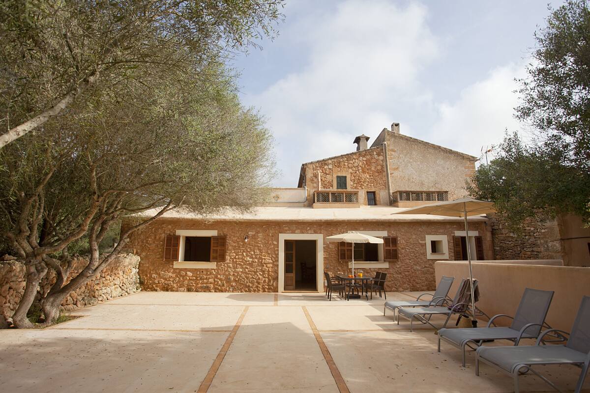Un bâtiment en pierre doté d’un balcon, une terrasse avec des fauteuils de jardin et un arbre.