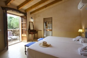 Ein Schlafzimmer mit einem großen Bett, einem Holztisch, einem Stuhl, einem Spiegel und einer offenen Tür zu einem Balkon mit einem Stuhl und einem Tisch.