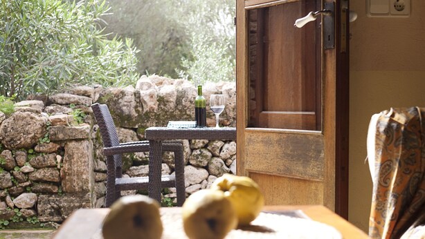 A table with a bottle and a glass, a chair, and a window with a view of greenery and a stone wall. - Agroturismo Finca Son Sureda (Manacor)