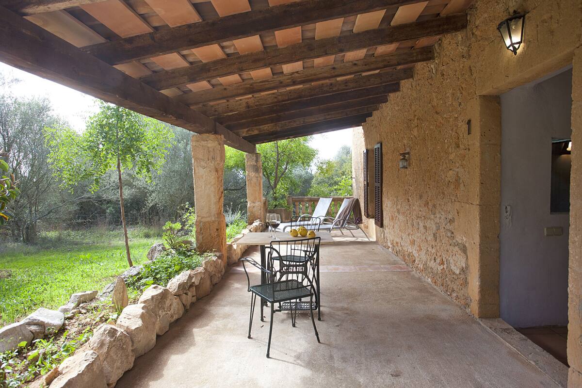 Un patio abrité, doté de murs en pierre, d’une table avec des chaises et offrant une vue sur la verdure environnante.