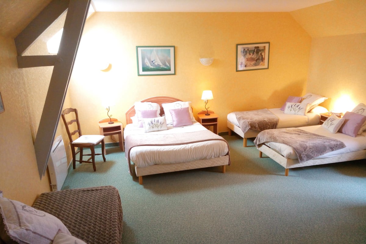 A room with two single beds, a double bed, a chair, a small table, and a lamp.