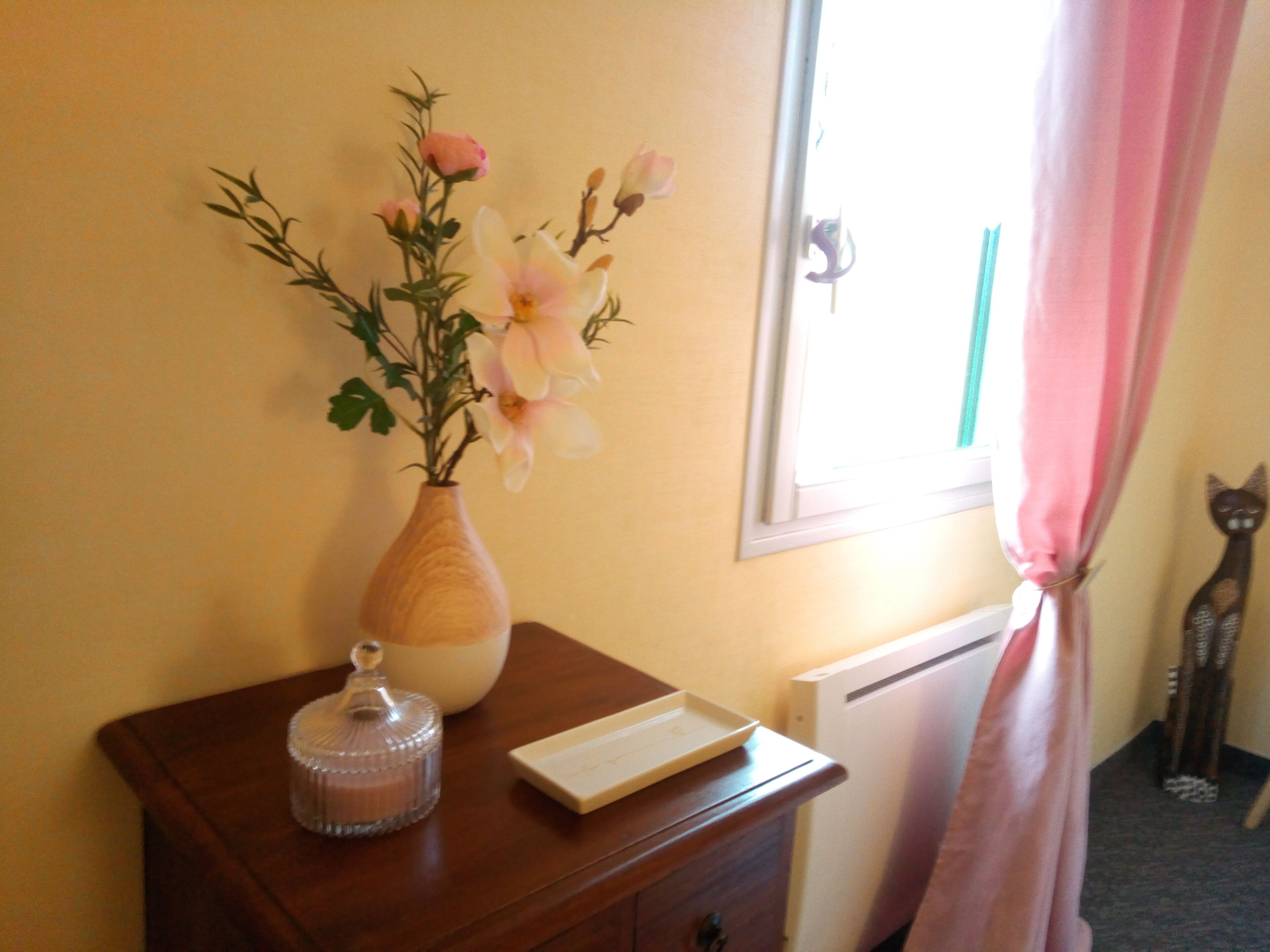 A wooden dresser with a vase of flowers, a candle, and a small tray.