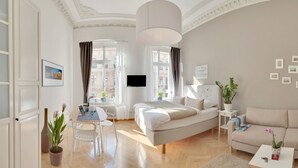 Moderni hotellihuone, jossa on sänky, sohva, ruokapöytä ja ruukkukasveja.
