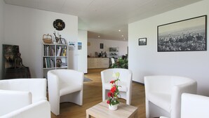 Una sala de estar moderna con muebles blancos, una estantería y un comedor al fondo.