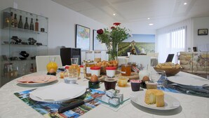 Una mesa de desayuno dispuesta con diversos alimentos y bebidas, un florero con flores y un cuadro en la pared.