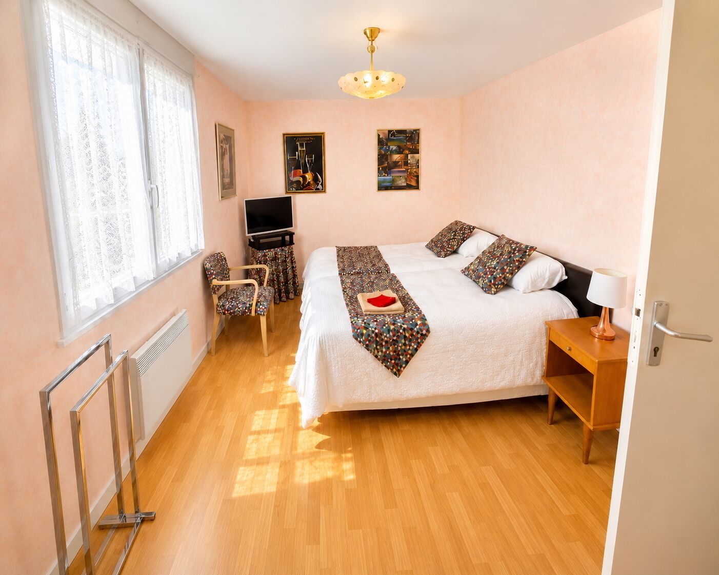 A hotel room with a bed, a TV, a chair, a desk, and a window with curtains.