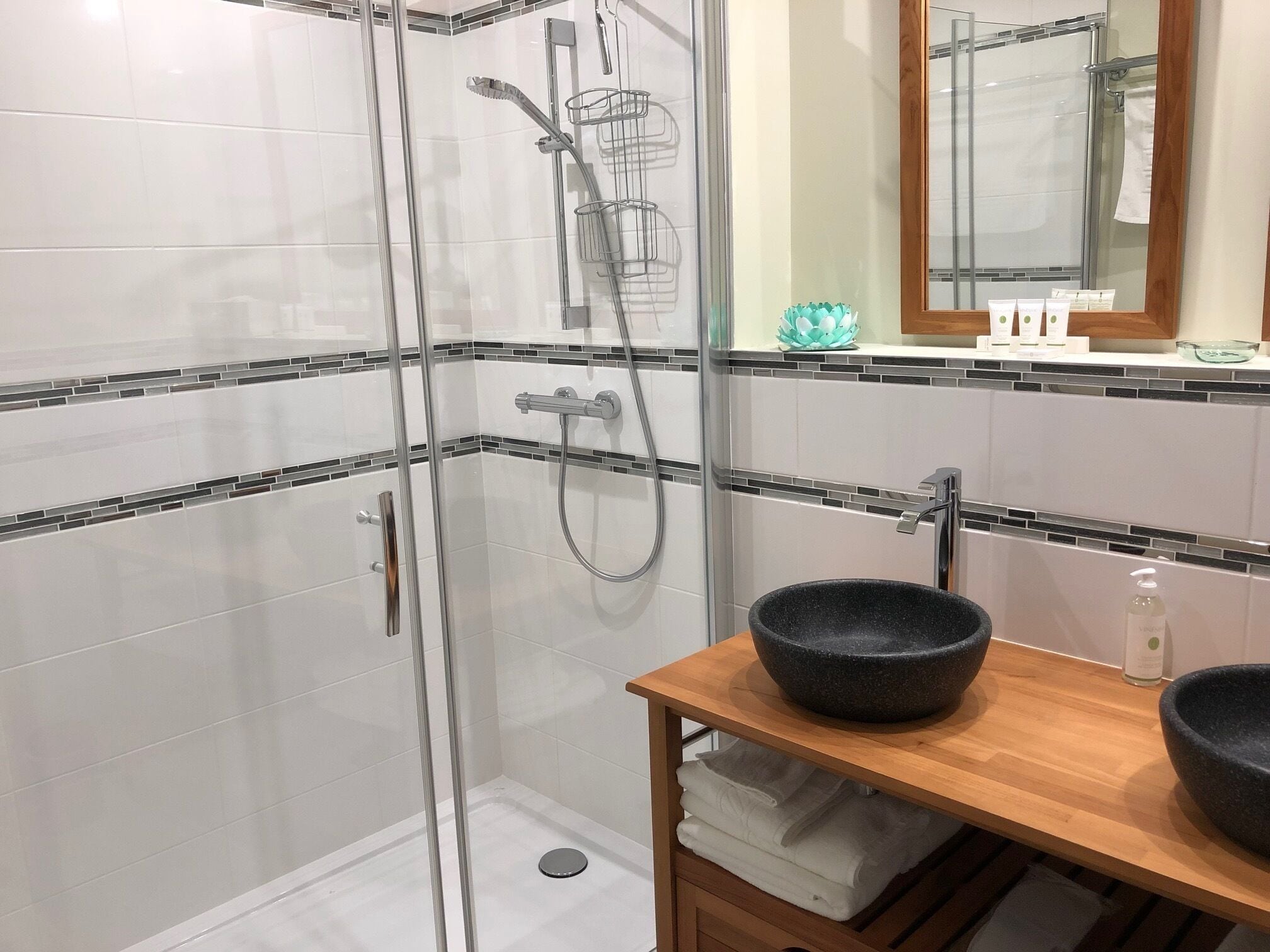 A modern bathroom with a glass-enclosed shower, a wooden vanity with two black bowls, and a mirror above the sink.