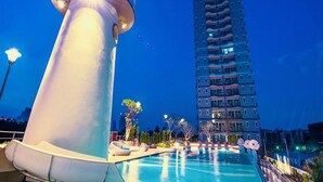 A swimming pool with lounge chairs and a tall building in the background. - Supalai Mare Pattaya Condo Sea View by Dome (Pattaya)