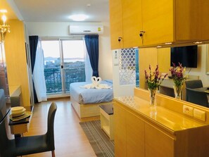 A hotel room with a bed, a desk, a chair, a dining table, a TV, and a view of the city.