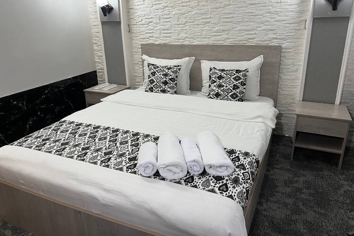 A hotel room with a bed, two nightstands, a headboard, and a patterned bedspread.