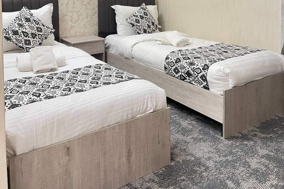 A hotel room with two beds, a wall-mounted air conditioner, and a patterned wallpaper.