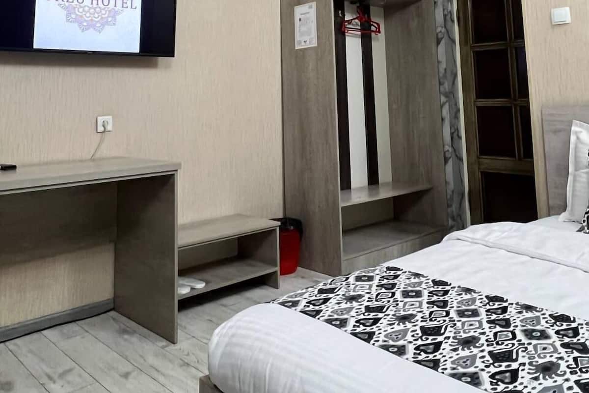A hotel room with a bed, a TV mounted on the wall, a wardrobe, and a desk.