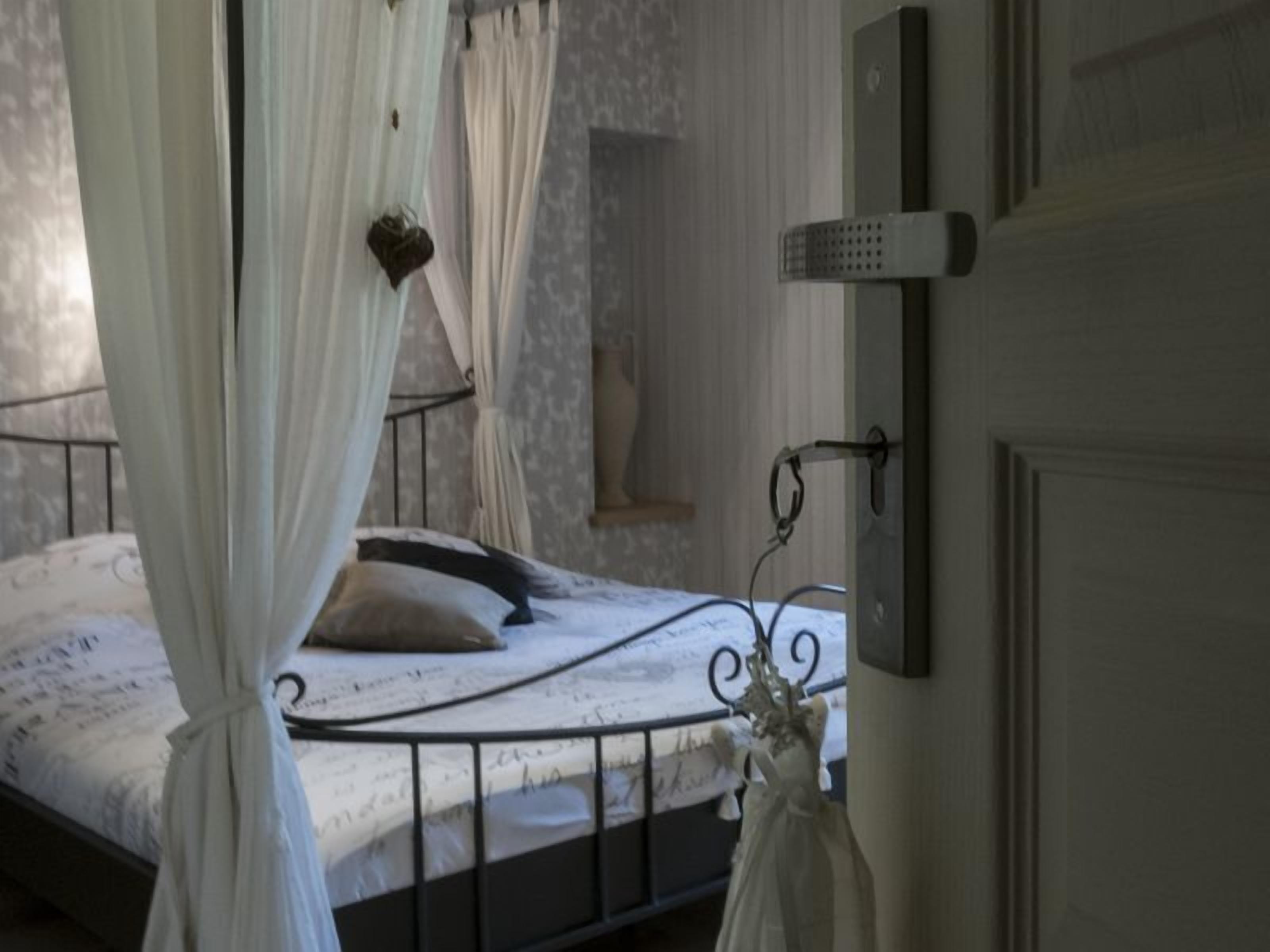 A bedroom with a bed, white curtains, and a bedside table.