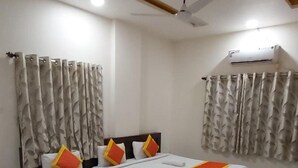 A modern hotel room with a large bed, curtains, a ceiling fan, and an air conditioning unit. - Hotel Radhika Inn (Trimbak)