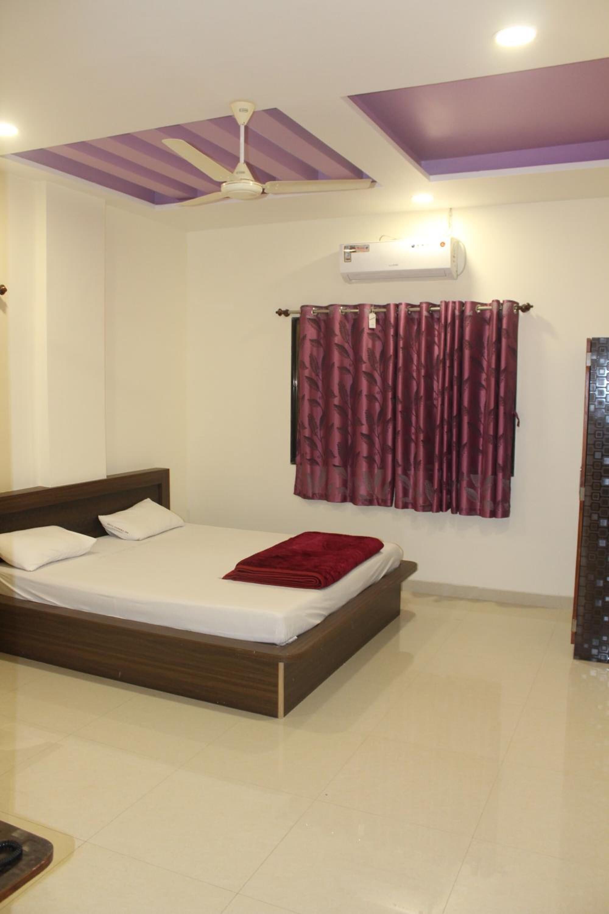 A bedroom with a bed, a ceiling fan, an air conditioning unit, and a window with curtains.