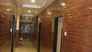 A corridor with wooden panel walls and a shiny tiled floor, leading to a door at the end. - Hotel Radhika Inn (Trimbak)