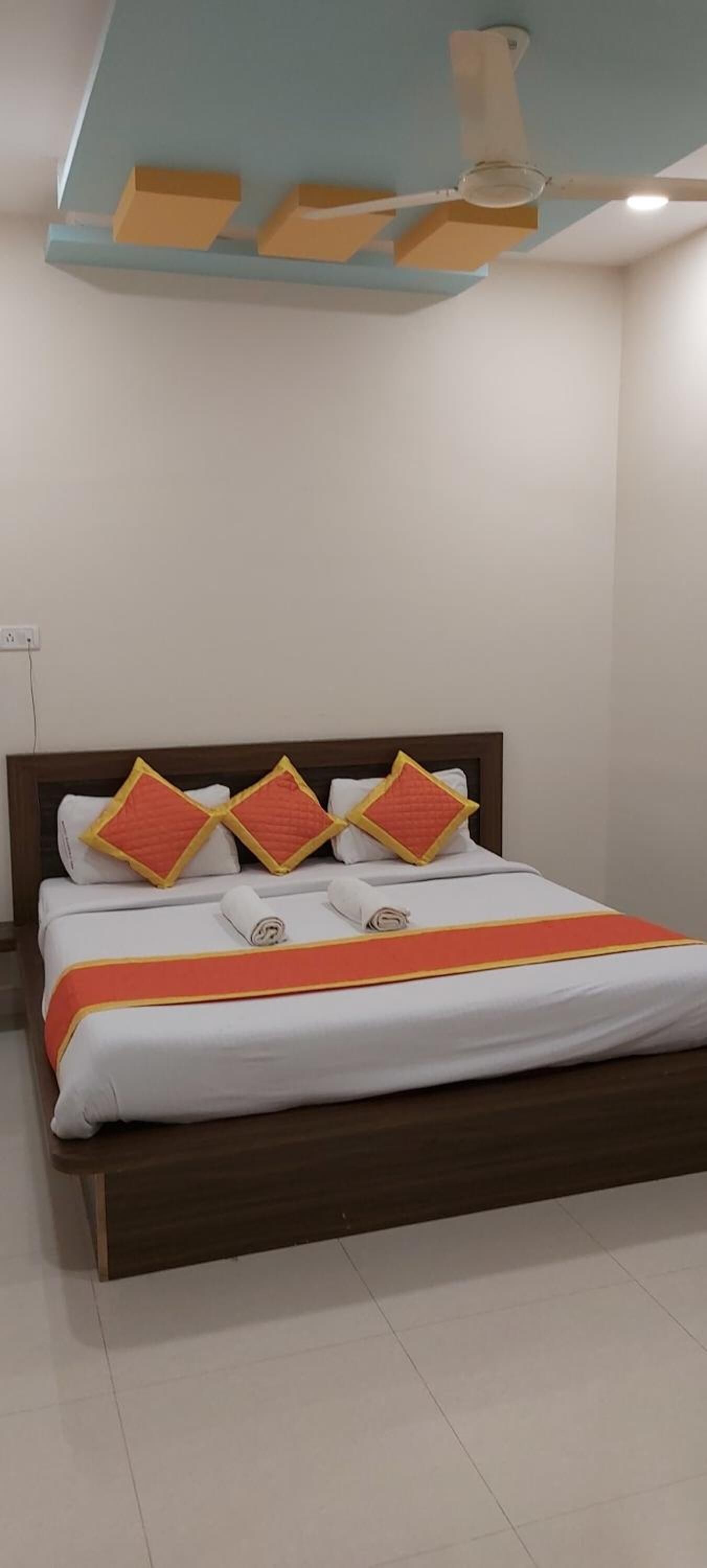 A neatly made bed with a wooden headboard, white bedding, and orange accents.